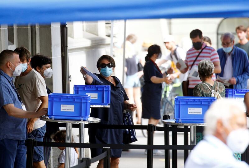 A woman throws an envelope into a box as people queue to cast their votes in a series of referendums in front of a ballot station at the Stadthaus administration building in Zurich, Switzerland June 13, 2021.  REUTERS/Arnd Wiegmann