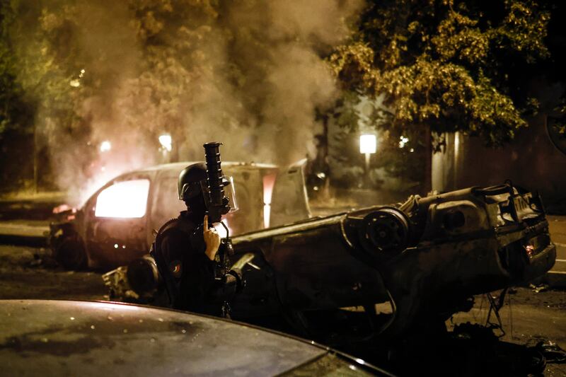 A car burns in the suburb as riot police pass. EPA