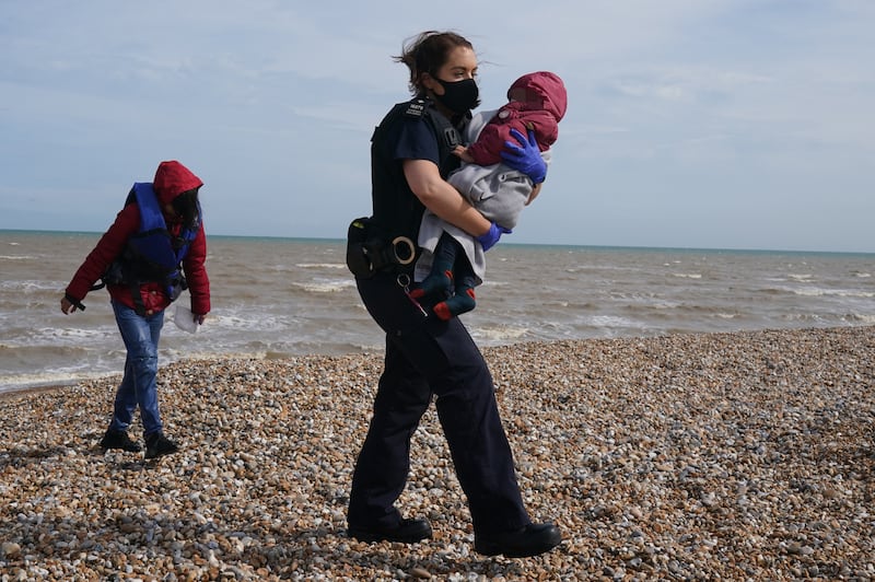 An officer from Immigration Enforcement carries a child along the beach in Dungeness. PA