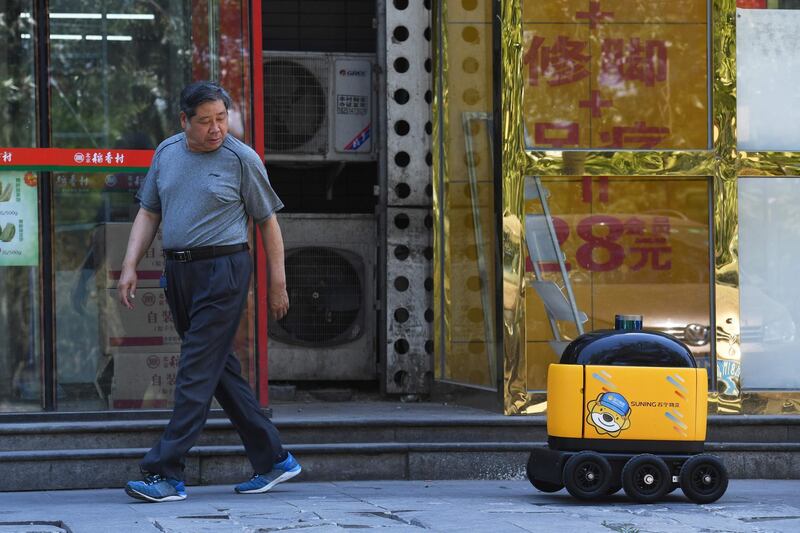 A man looks back at a Zhen Robotics delivery robot as it makes its way back to a supermarket after making a delivery during a demonstration in Beijing. Along a quiet residential street on the outer edges of Beijing, a yellow and black cube about the size of a small washing machine trundles leisurely to its destination. This "little yellow horse" is an autonomous delivery robot, ferrying daily essentials like drinks, fruit and snacks from the local store to the residents of the "Kafka" compound in the Chinese capital.
 - TO GO WITH AFP STORY CHINA-TECHNOLOGY-ROBOTS-CONSUMER-SCIENCE,FEATURE BY LUDOVIC EHRET
 / AFP / GREG BAKER / TO GO WITH AFP STORY CHINA-TECHNOLOGY-ROBOTS-CONSUMER-SCIENCE,FEATURE BY LUDOVIC EHRET
