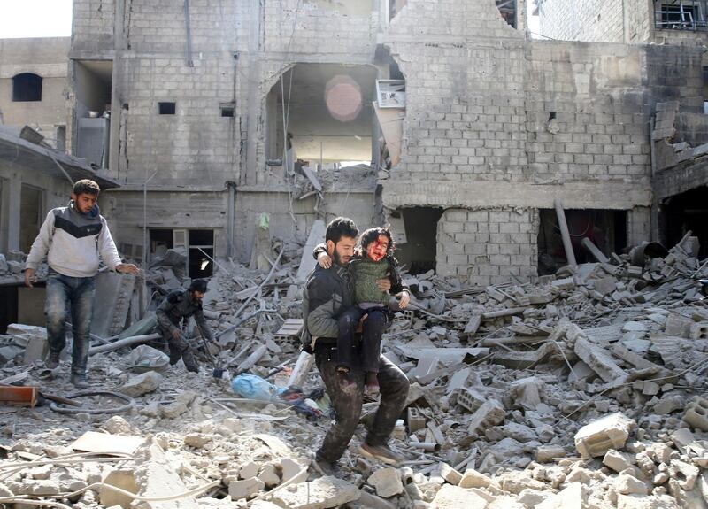 ATTENTION EDITORS - VISUAL COVERAGE OF SCENES OF INJURY OR DEATH A man carries an injured boy as he walks on rubble of damaged buildings in the rebel held besieged town of Hamouriyeh, eastern Ghouta, near Damascus, Syria, February 21, 2018. REUTERS/Bassam Khabieh   TEMPLATE OUT
