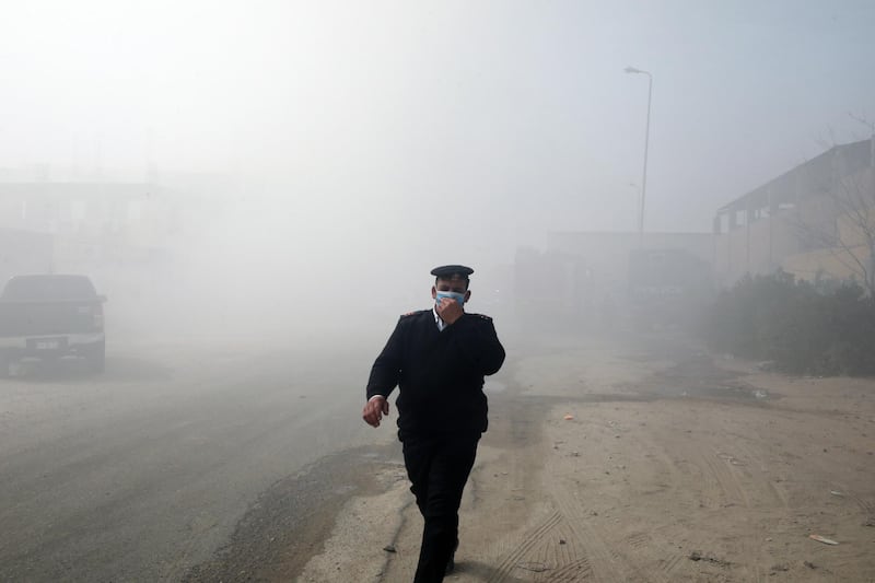 epa09067790 An Egyptian policeman walks amid smoke rising from a fire at a textile factory in Obour industrial district, outskirts of Cairo, Egypt, 11 March 2021. At least 20 people died and 24 were injured after a fire broke out in a textile factory northeast of Cairo, local authorities reported after controlling the fire.  EPA/KHALED ELFIQI
