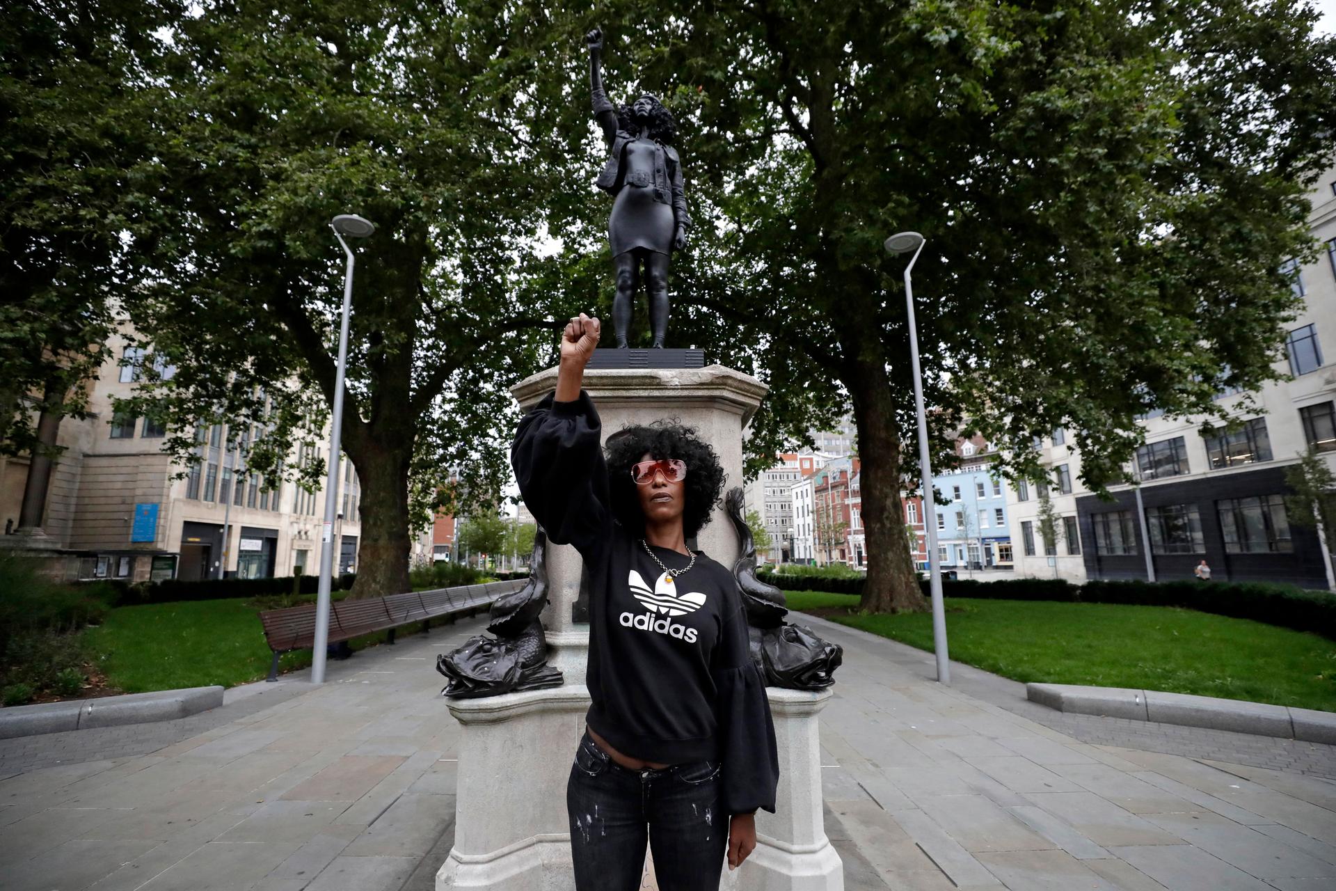 Jen Reid poses for photographs in front of the new black resin and steel statue portraying her, entitled "A Surge of Power (Jen Reid) 2020" by artist Marc Quinn after the statue was put up this morning on the empty plinth of the toppled statue of 17th century slave trader Edward Colston, which was pulled down during a Black Lives Matter protest in Bristol, England, Wednesday, July 15, 2020. On June 7 anti-racism demonstrators pulled the 18-foot (5.5 meter) bronze likeness of Colston down, dragged it to the nearby harbor and dumped it in the River Avon — sparking both delight and dismay in Britain and beyond. (AP Photo/Matt Dunham)