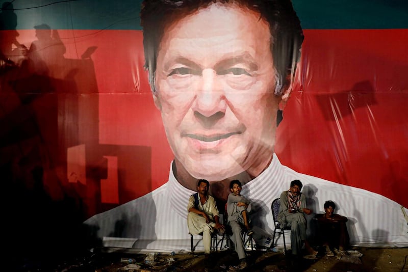 FILE PHOTO: Labourers, who set up the venue, sit under a wall with a billboard displaying a photo of Imran Khan, chairman of the Pakistan Tehreek-e-Insaf (PTI), political party, as they listen to him during a campaign rally ahead of general elections in Karachi, Pakistan July 22, 2018. REUTERS/Akhtar Soomro/File Photo