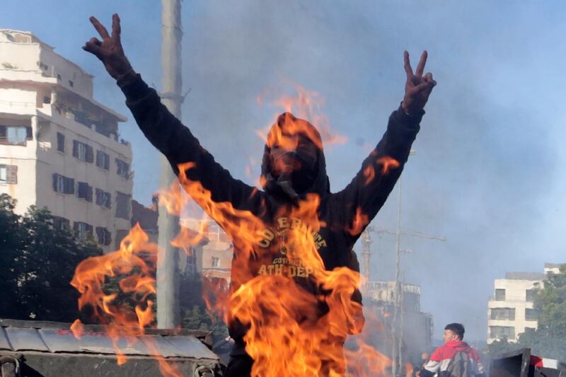 An anti-government protester shouts slogans in front of a fire set by demonstrators to block the main highway that link east and west Beirut, Lebanon, Tuesday, Jan. 14, 2020. Lebanese protesters have blocked several roads around the capital of Beirut and other cities and towns in renewed rallies against the ruling elite they say has failed to address the economy's downward spiral. (AP Photo/Hassan Ammar)