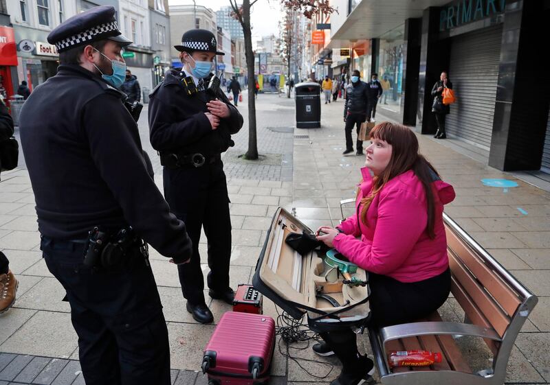 Police officers speak to a busker as they patrol to enforce lockdown measures in the town centre of Ilford. AP Photo