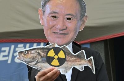 A South Korean environmental activist wearing a mask of Japan's Prime Minister Yoshihide Suga holds a picture of a fish with a radioactivity warning sign during a protest against Japan's decision on releasing Fukushima wastewater, near the Japanese embassy in Seoul on April 13, 2021. / AFP / Jung Yeon-je
