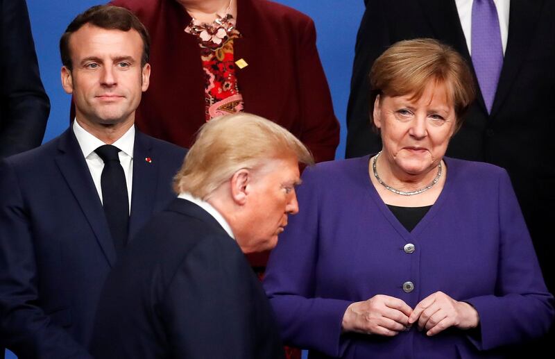 TOPSHOT - France's President Emmanuel Macron (L) and Germany's Chancellor Angela Merkel (R) look at US President Donald Trump (C) walking past them during a family photo as part of the NATO summit at the Grove hotel in Watford, northeast of London on December 4, 2019. / AFP / POOL / CHRISTIAN HARTMANN
