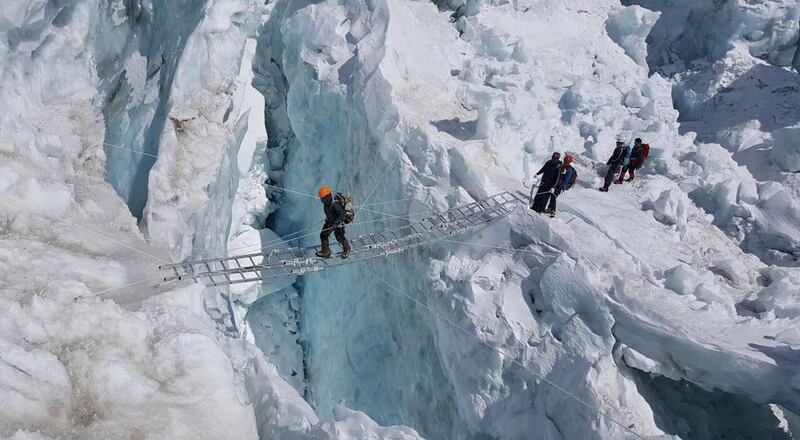 Members of the Armed Forces cross a crevasse on ladders in the Khumbu Icefall.