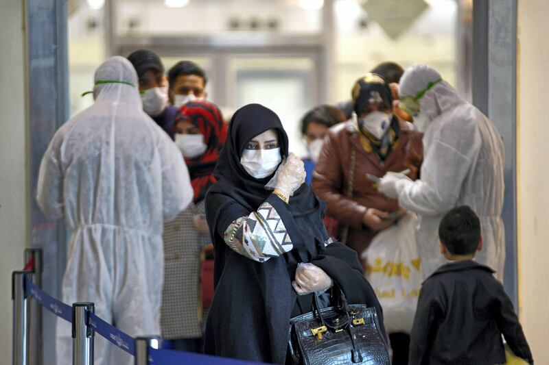 TOPSHOT - Medical staff in protective gears distribute information sheets to Iraqi passengers returning from Iran at Najaf International Airport on March 5, 2020. Iraqi health authorities announced the country's first two deaths from the new coronavirus, one in the capital Baghdad and the other in the autonomous Kurdish region. / AFP / Haidar HAMDANI
