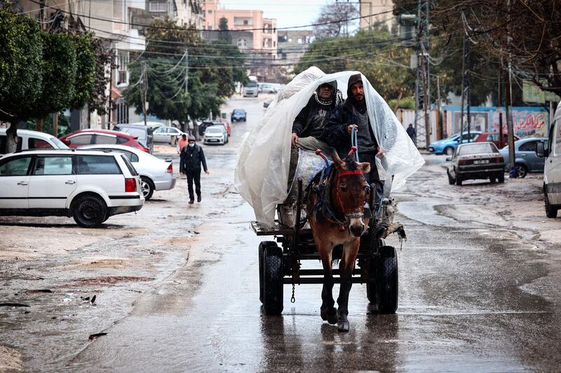 Men take cover from the rain under a plastic sheet as they ride a donkey-pulled cart in Gaza City. AFP