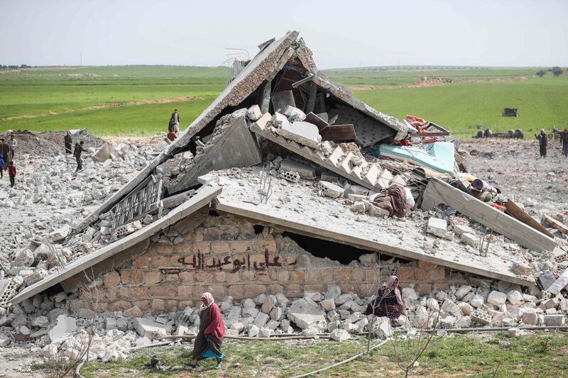 A displaced Syrian woman walks past a destroyed poultry farm which was part of a makeshift camp following reported air strikes on the outskirts of the jihadist-held city of Idlib, on March 13, 2019.   / AFP / OMAR HAJ KADOUR
