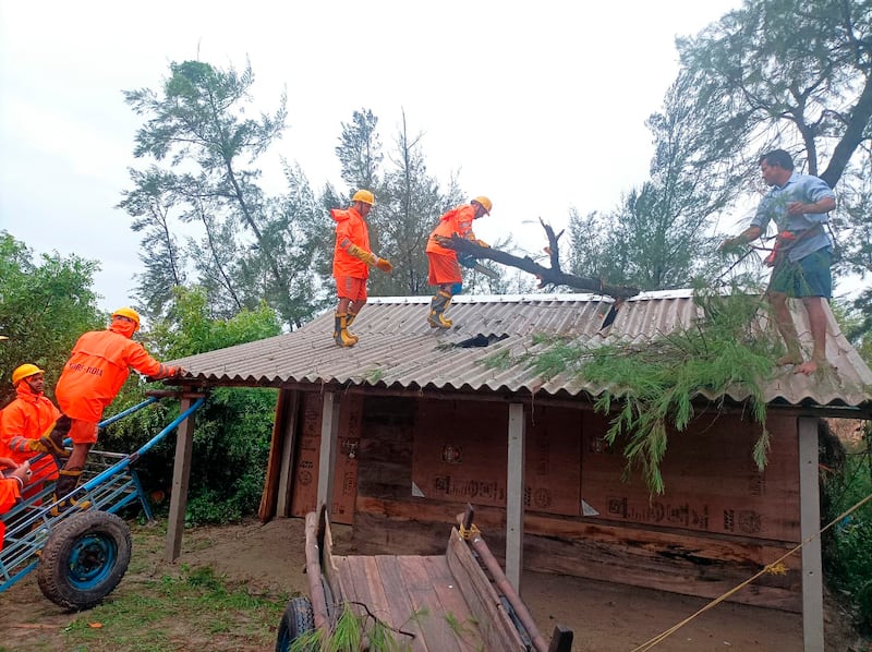India's National Disaster Response Force members remove tree branches off the roof of a house in West Bengal state. AP