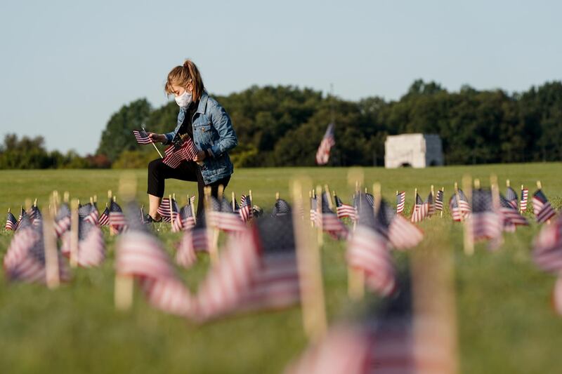 A volunteer places American flags representing some of the 200,000 lives lost in the United States in the coronavirus disease (Covid-19) pandemic on the National Mall in Washington, DC, USA. Reuters