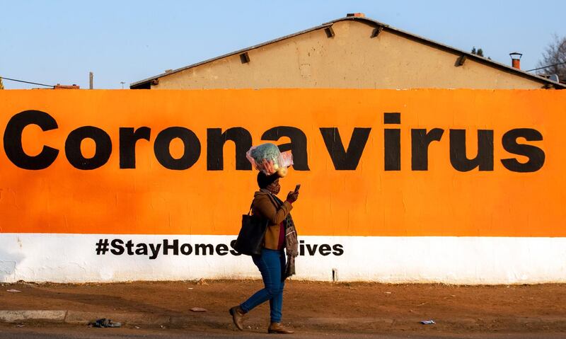 A woman wearing a face mask whilst carrying a bag of vegetables atop her head, walks past a wall with COVID-19 message urging people to stay home in Soweto, South Africa, Friday, June 19, 2020. (AP Photo/Themba Hadebe)