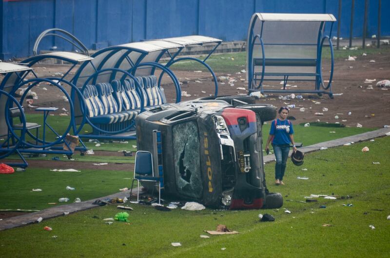 A woman walks past a damaged police vehicle inside Kanjuruhan Stadium. EPA