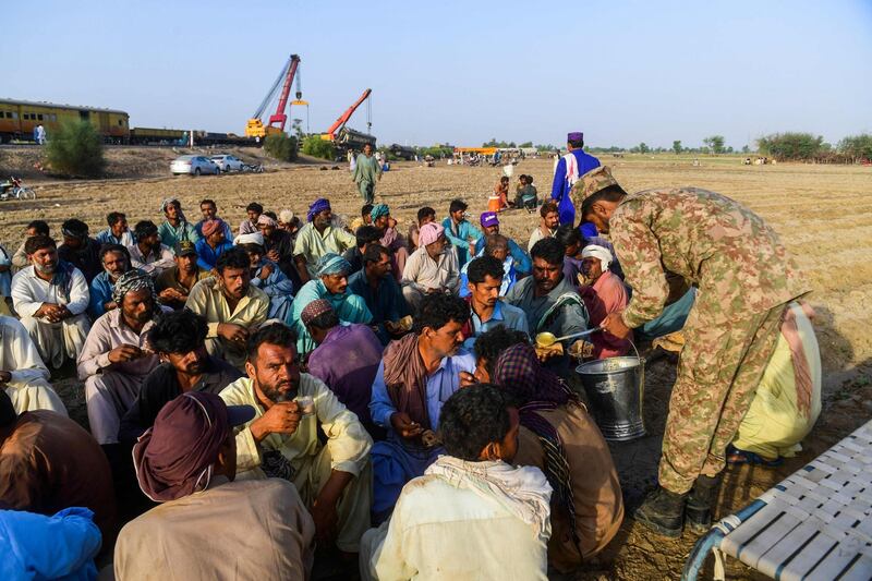 A soldier serves breakfast to workers before they start cleaning wreckage from the railway line in Ghotki district, Pakistan, a day after a packed inter-city train ploughed into another express that had derailed, killing at least 40 people. AFP
