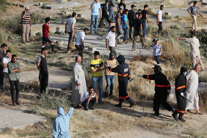 Palestinian policemen in protective suits hold people back during the burial of a woman who has died after contracting the coronavirus in the southern Gaza Strip. Reuters