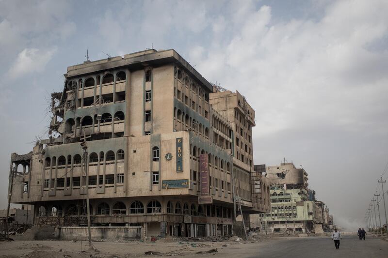 MOSUL, IRAQ - NOVEMBER 06:  People walk on a road next to the destroyed Baghdad Hotel in West Mosul on November 6, 2017 in Mosul, Iraq. Five months after Mosul, Iraq's second-largest city was liberated from ISIL in a nine-month long battle, residents have returned to the destroyed city to rebuild their lives. After more than two years of ISIL occupation, savage fighting, airstrikes and as ISIL fighters retreated they intentionally destroyed remaining key infrastructure such as bridges, government buildings, water and sewage facilities and neighborhoods laced with booby traps and homemade bombs leaving the city in ruins. Despite the damage residents have hastily returned and managed to setup temporary shops, homes and services to help bring the city back to life. In West Mosul, home to the Old City, more than 32,000 homes were destroyed and a recent report from the U.N. estimates repairing Mosul's basic infrastructure will cost more than $1 billion and take years to complete. (Photo by Chris McGrath/Getty Images)