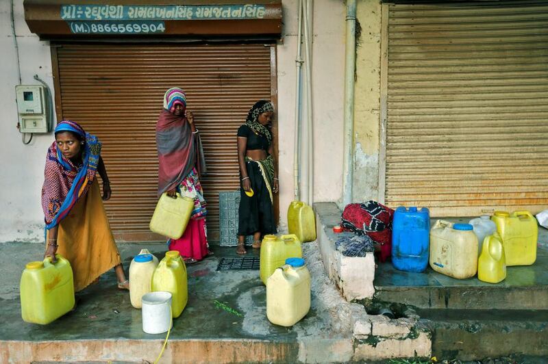 Women fill water containers from an underground tank beside closed shops on the outskirts of Ahmedabad.  Amit Dave / Reuters