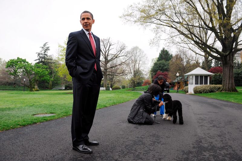 Barack Obama speaks to members of the press while Michelle Obama and their daughter Malia play with Bo in April 2009. EPA