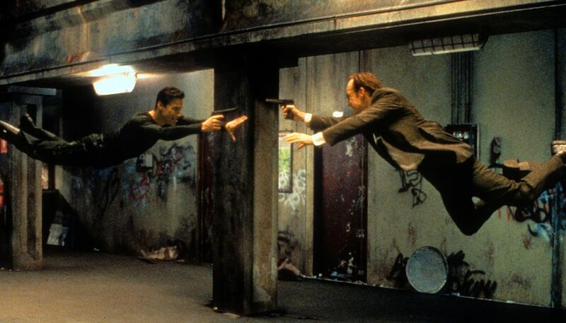 Keanu Reeves and Hugo Weaving pointing guns at each other in a scene from the film 'The Matrix', 1999. (Photo by Warner Brothers/Getty Images)