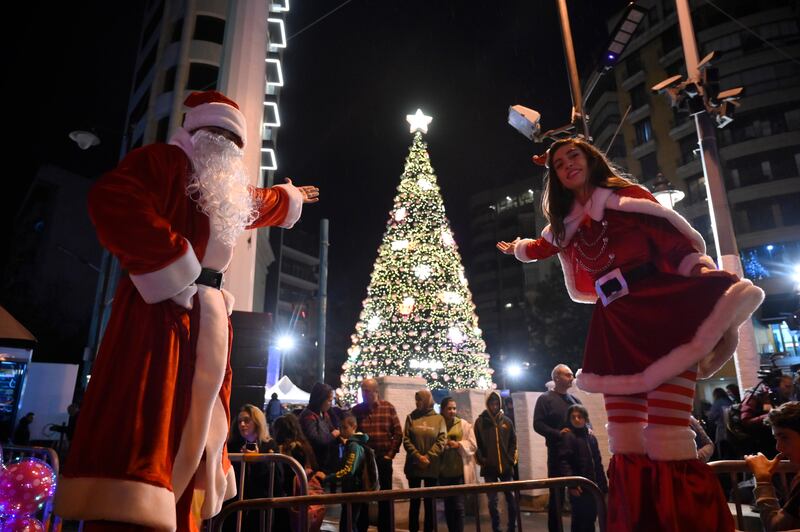 People dress as Santa Clauses pose in front of the 17-meter-high Christmas tree, which has been officially lit up at the Ashrafieh area in Beirut, Lebanon, 07 December 2022.   EPA / WAEL HAMZEH