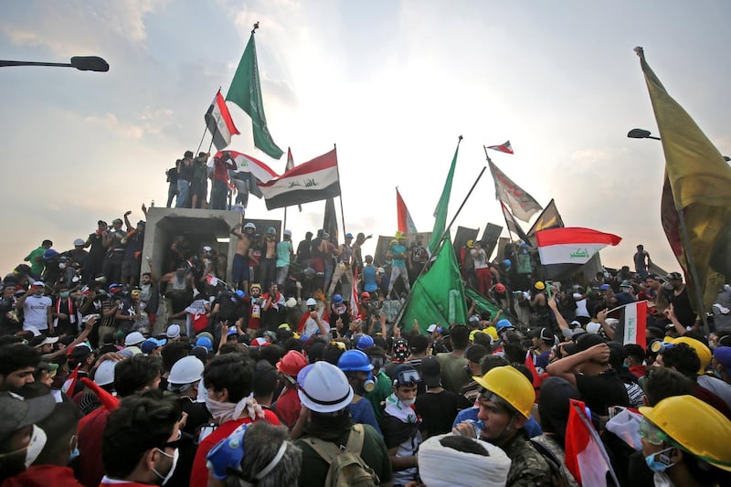 Protesters wave national flags as they stand on top of concrete barriers across Al Jumhuriya Bridge in Baghdad during anti-government protests. AFP