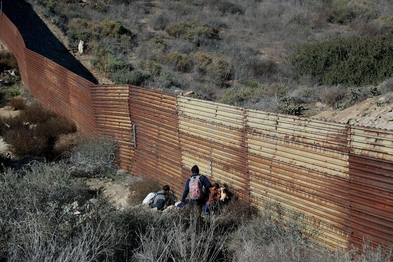 Migrant family members cross under the US border wall, aided by two local guides, in Tijuana, Mexico.. AP