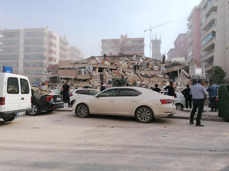 People near a collapsed building in Izmir. According to Turkish media reports dozens of buildings were destroyed in the earthquake. EPA