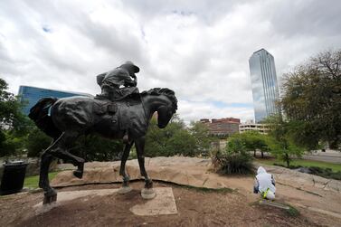 A statue on Pioneer Plaza faces towards downtown Dallas as Edwin Anzelmo, right, waits for a ride after his work shift, Tuesday, March 31, 2020. AP