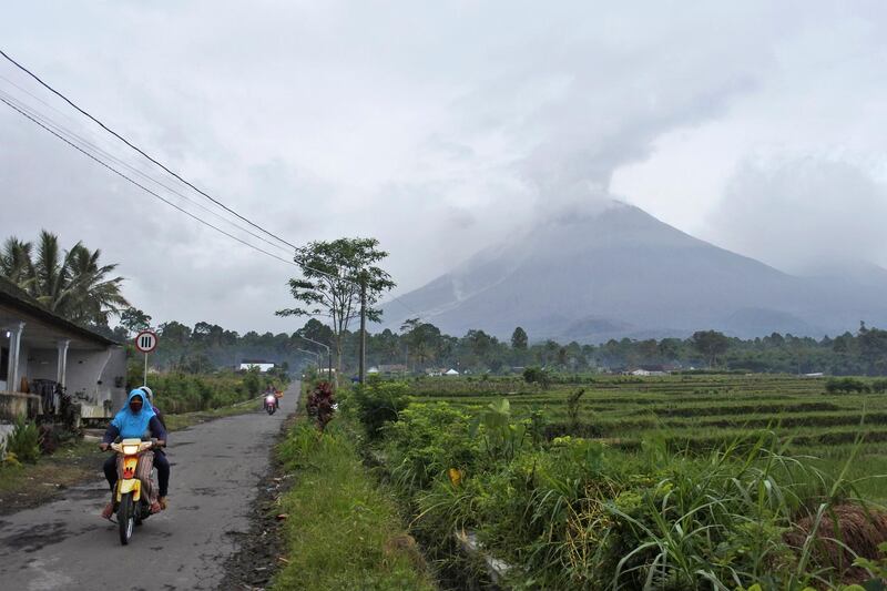 Motorists ride on a village road as Mount Semeru is seen spewing volcanic smoke. AP