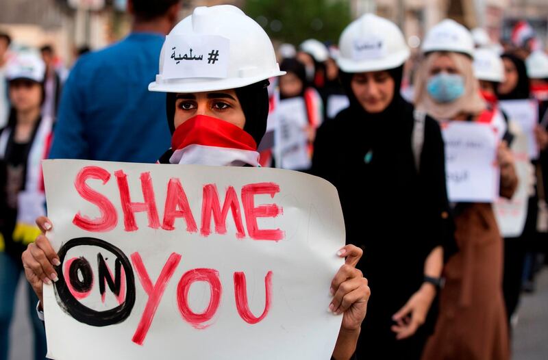 An Iraqi woman protester wearing a construction helmet adorned with the word "#Peaceful" in Arabic marches with a sign during an anti-government demonstration in the southern Iraqi city of Basra.  AFP