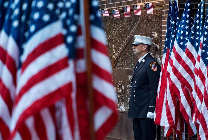 A New York City firefighter stands at attention by a memorial at the side of a firehouse adjacent to One World Trade Center and the 9/11 Memorial site. AP Photo