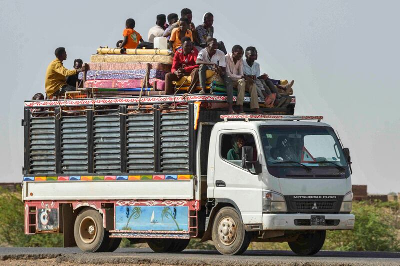 People ride with furniture and other items atop a truck moving along a road from Khartoum to Wad Madani