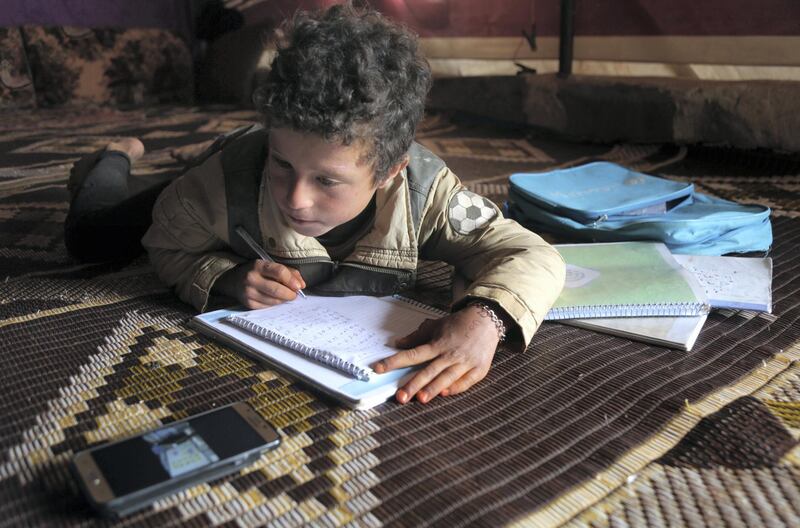 A young pupil follows a lesson on a mobile telephone inside a tent, in a camp for displaced Syrians in the village of Kafr Yahmoul in the northwestern Idlib province, amid the coronavirus pandemic on April 3, 2020. - Like in much of the world, educators in Syria are taking classes online after the country's various regions sent pupils home hoping to stem the COVID-19 pandemic. 
But distance learning is no small feat in a country battered by nine years of war, where fighting has displaced millions and the electricity supply is sporadic at best. (Photo by Aref TAMMAWI / AFP)