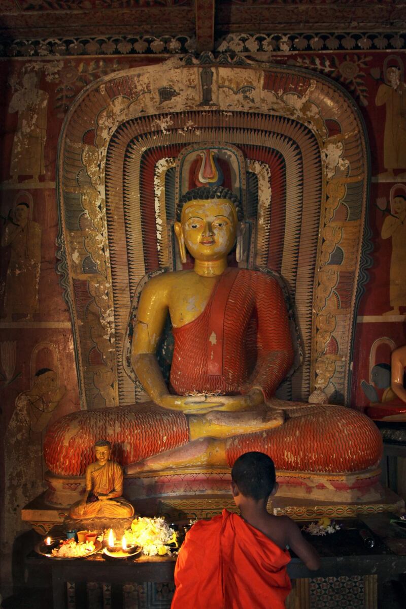 epa03641512 A saffron robed Sri Lankan 'samanera' or novice monk places offerings at the foot of an ancient Buddha image at a temple at Heiyanthuduwa in Biyagama on the outskirts of Colombo, Sri Lanka, 26 March 2013. This Buddhist temple is believed to have been constructed during the Kandyan era in the village of Heiyanthuduwa in Biyagama during the reign of King Rajasinghe II between 1635-1687 AD.  EPA/M.A.PUSHPA KUMARA *** Local Caption ***  03641512.jpg