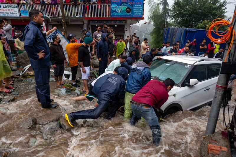 People in India help to dislodge a car stuck due to flash floods in Bhagsunag, Himachal Pradesh.