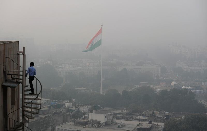 An Indian man walks up to the stairs as Delhi's sky line is seen enveloped in smog and dust in New Delhi, India. AP Photo