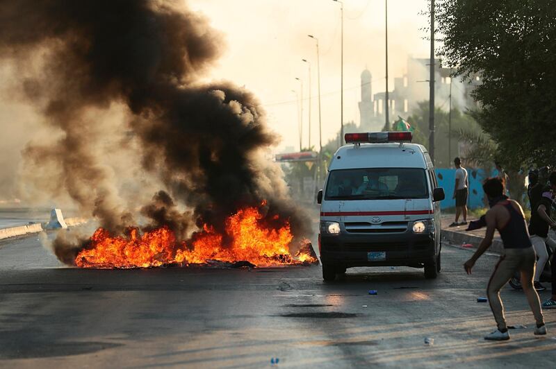 Anti-government protesters set fires and close a street while the ambulance transports injured protesters during a demonstration in Baghdad, Iraq.  AP