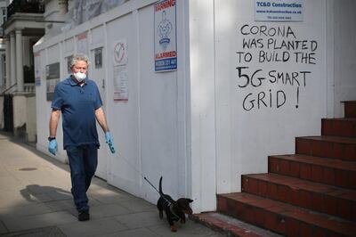 A man wearing a protective mask and gloves walks his dog past graffiti that reads "Corona was planted to build the 5G smart grid!" in Kensington, as the spread of the coronavirus disease (COVID-19) continues, London, Britain, April 16, 2020. REUTERS/Hannah McKay