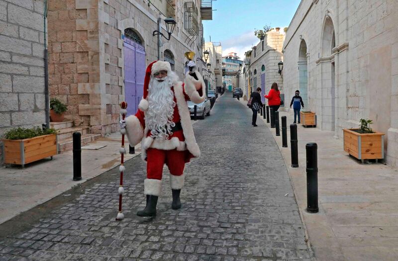A Palestinian man dressed as Santa Claus walks along an almost deserted street in the occupied West Bank town of Bethlehem, ahead of Christmas, on December 23, 2020.  Deprived of its usual tourist influx by the pandemic, Bethlehem will celebrate a quiet Christmas this year that is less about commerce and more about religion, says its parish priest. / AFP / HAZEM BADER
