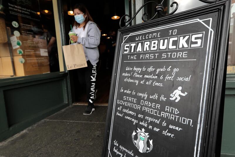 A customer walks out of the first Starbucks store, Tuesday, July 7, 2020, at Pike Place Market in Seattle. Tuesday was the first day of a new statewide order that requires people to wear masks or other facial coverings inside businesses in hopes of slowing the spread of the coronavirus. Business owners who fail to refuse service to customers who don't wear masks can face fines or lose their business license, but some business owners have raised concerns about turning away customers. (AP Photo/Ted S. Warren)