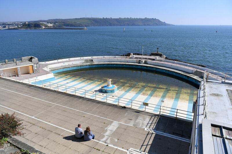 PLYMOUTH, ENGLAND - APRIL 08: A couple sit in the sunshine overlooking the closed Tinside Lido on April 08, 2020 in Plymouth, England. There have been around 50,000 reported cases of the COVID-19 coronavirus in the United Kingdom and 5,000 deaths. The country is in its third week of lockdown measures aimed at slowing the spread of the virus. (Photo by Dan Mullan/Getty Images)