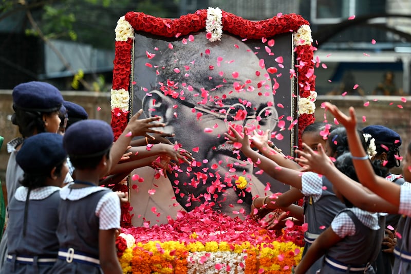 Indian school children throws rose flower petals over a portrait of Mahatma Gandhi to pay their tribute on the death anniversary of the Indian founding father, in Chennai on January 30, 2024.  The death anniversary of Gandhi, who is widely known in India as Bapu (father), is also observed as Martyrs' Day in the country.  (Photo by R. Satish BABU  /  AFP)