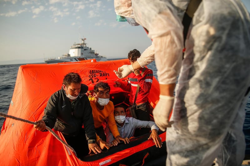 Turkish coast guards officers on their vessel, wearing protective gear to help prevent the spread of coronavirus, talk to migrants on a life raft during a rescue operation in the Aegean Sea, between Turkey and Greece, Saturday, Sept. 12, 2020. Turkey is accusing Greece of large-scale pushbacks at sea â€” summary deportations without access to asylum procedures, in violation of international law. The Turkish coast guard says it rescued over 300 migrants "pushed back by Greek elements to Turkish waters" this month alone. Greece denies the allegations and accuses Ankara of weaponizing migrants. (AP Photo/Emrah Gurel)