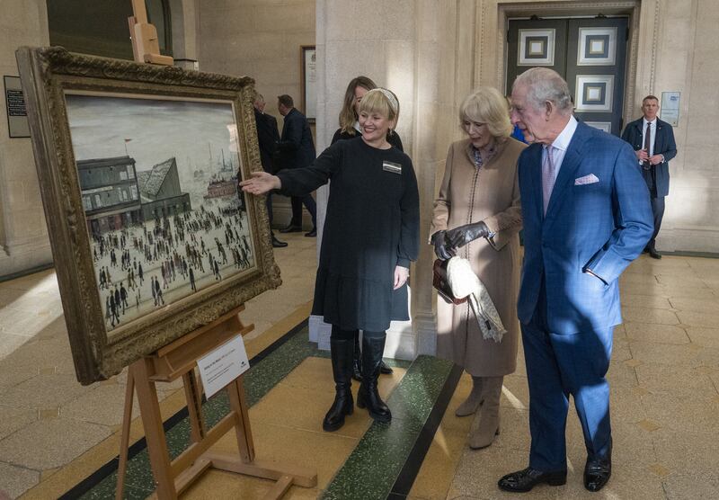 King Charles III and the Queen Consort views L S Lowry's Going to the Match painting during a visit to Bolton Town Hall.