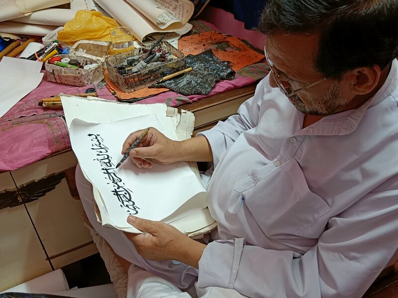 The calligrapher keeps his wooden dip pens, a set of inks and a small box containing other tools next to him as he works. 