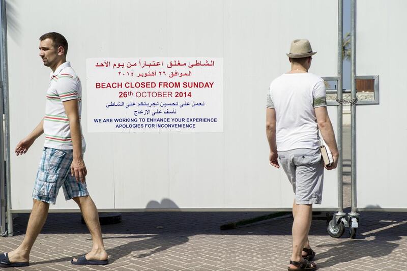 Visitors pass a sign on a wall used to fence off Jumeirah One Beach that alerts people to the closure. Antonie Robertson / The National