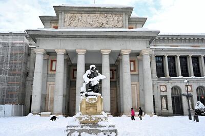 People walk their dog outside the Prado Museum in Madrid on January 10, 2021. - Snowstorms in Spain left three people dead and caused chaos across much of the country, trapping motorists and shutting down the capital's air and rail links. (Photo by Gabriel BOUYS / AFP)